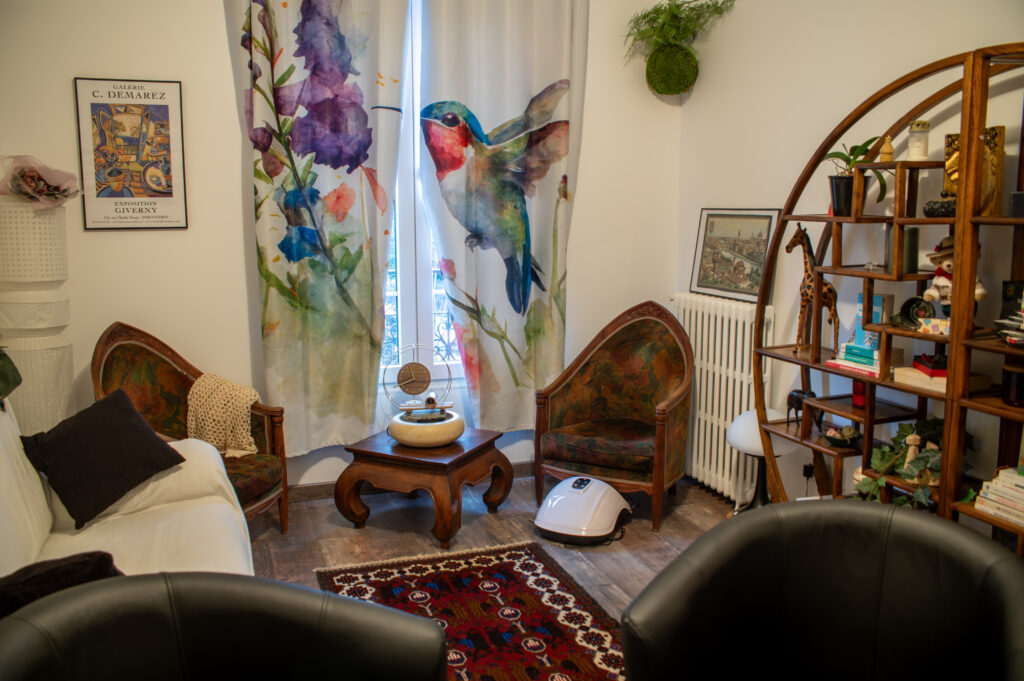 Le salon du cabinet de Péline au Raincy, avec fauteuils, rideaux aux motifs d’oiseaux et bibliothèque
